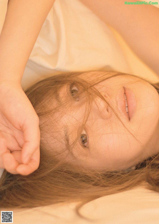 A young girl laying on a bed with her hands on her head.