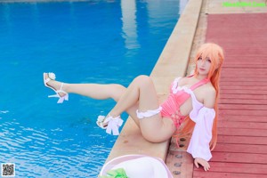 A woman in a pink bikini sitting by a swimming pool.