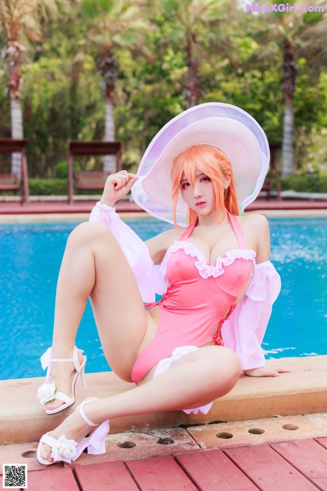 A woman in a pink bathing suit and white hat sitting by a pool.