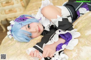 A woman in a maid outfit sitting on a bed.