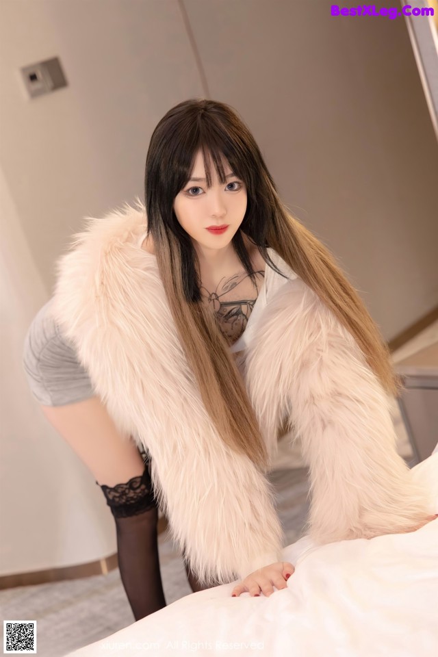 A woman in a fur coat posing on a bed.