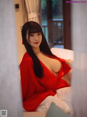 A naked asian woman in a red dress sitting on a bed.