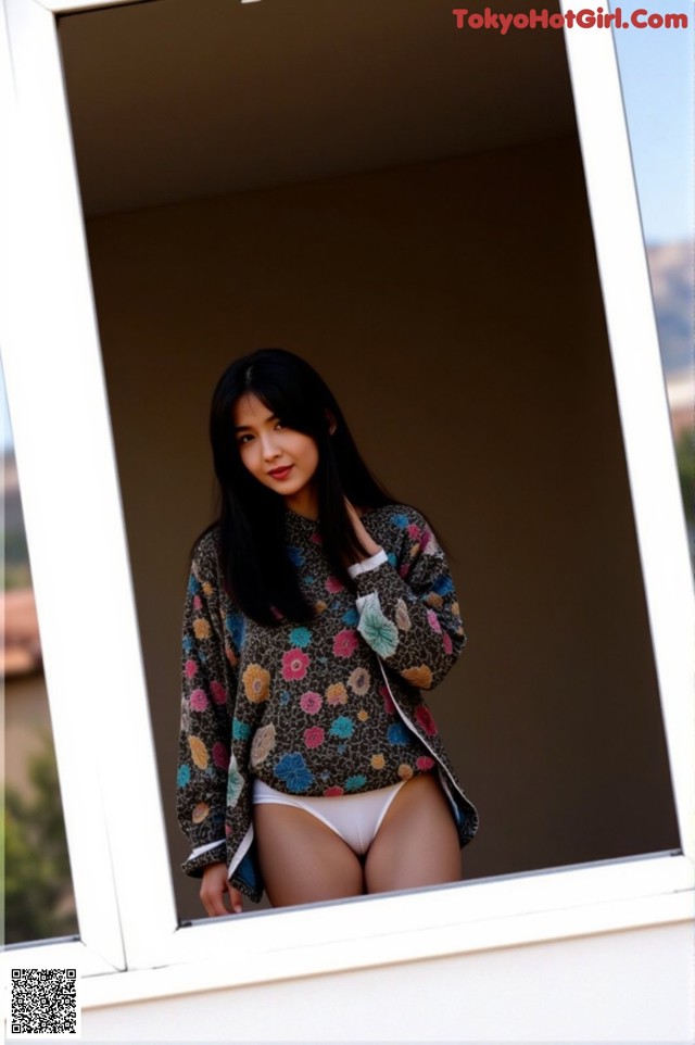 A woman in a floral shirt is looking out of a window.