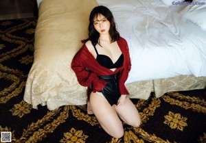 A woman in a black bra and panties sitting on a bed.