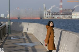 A woman sitting on a bench wearing a brown coat.