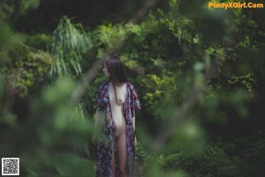 A naked woman standing in the middle of a forest.