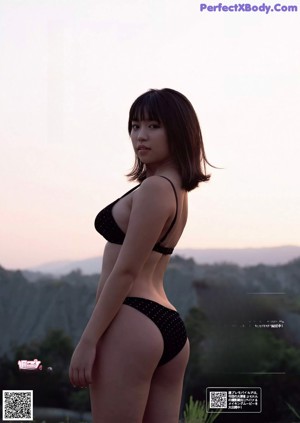 A woman in a black bikini standing in a field.