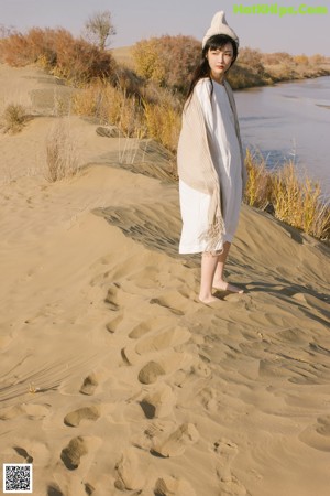 A woman leaning against a tree on the beach.