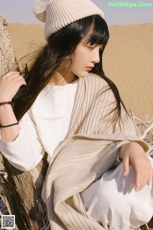 A woman sitting on top of a sandy beach.