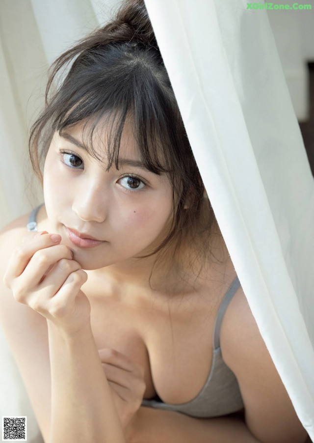 A woman in a gray tank top leaning against a white curtain.