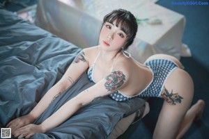 A woman in a blue and white polka dot bathing suit sitting on a bed.