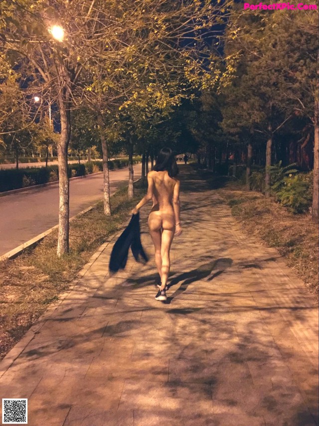 A naked woman walking down a sidewalk at night.