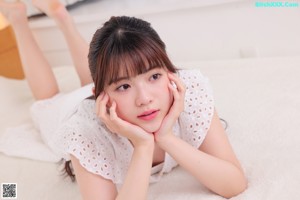 A woman in a white dress sitting on a bed.