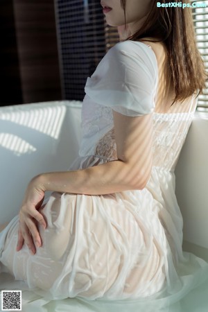 A woman sitting in a bathtub in a white dress.